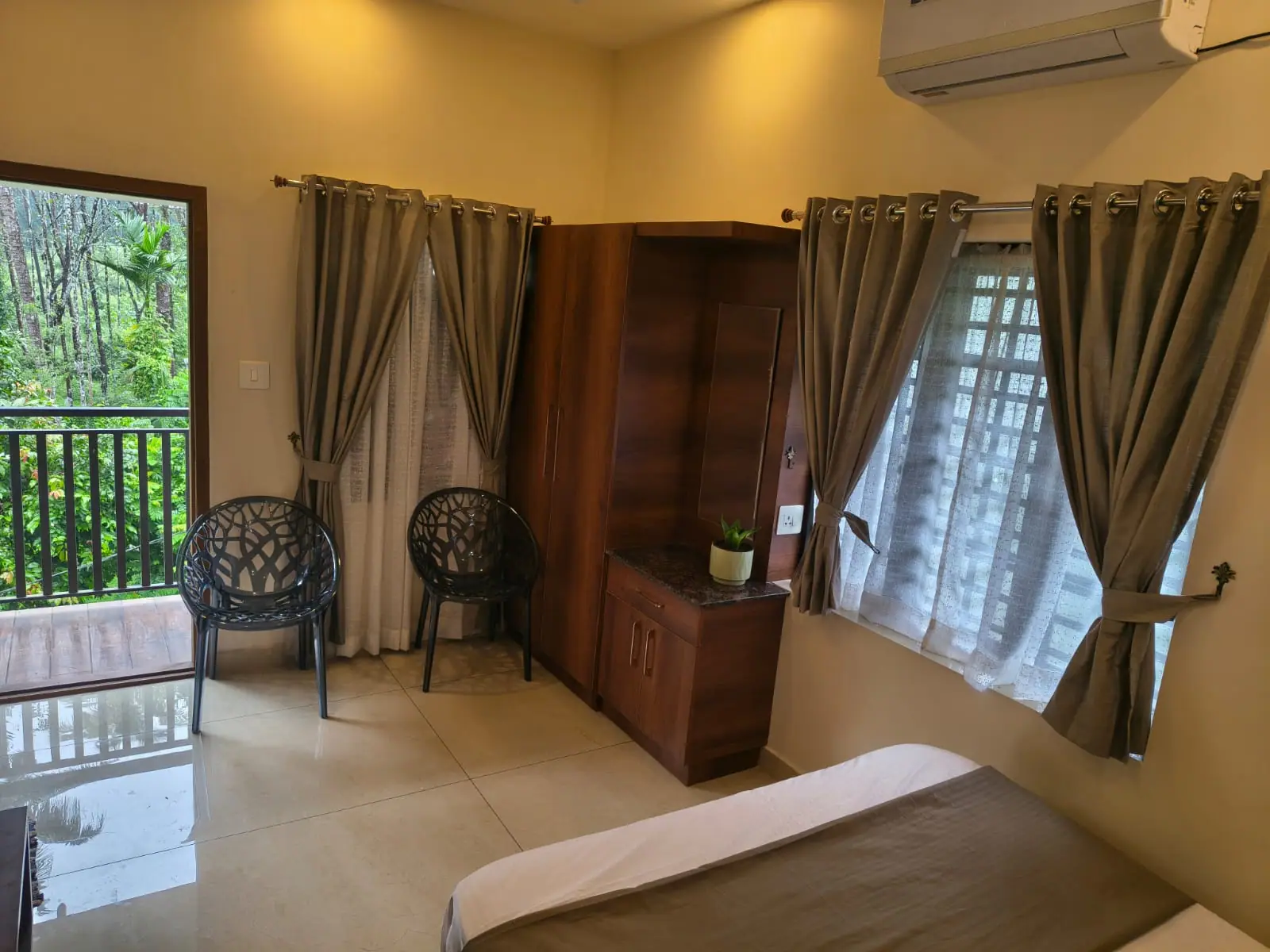 Bedroom at Nyra Thottam with a double bed, wooden wardrobe and a glass door opening to a balcony overlooking greenery