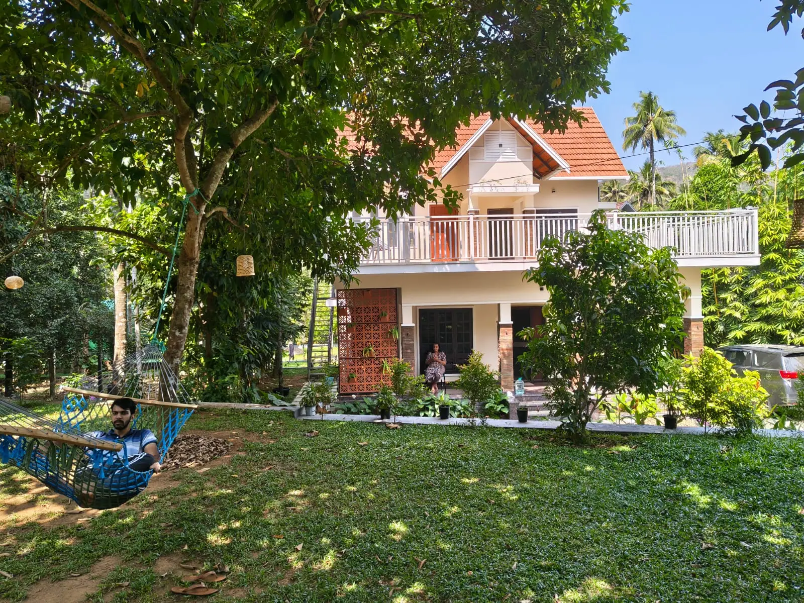 Front lawn of Nyra Thottam on a sunny day, with a hammock strung under a large shade tree and the villa behind